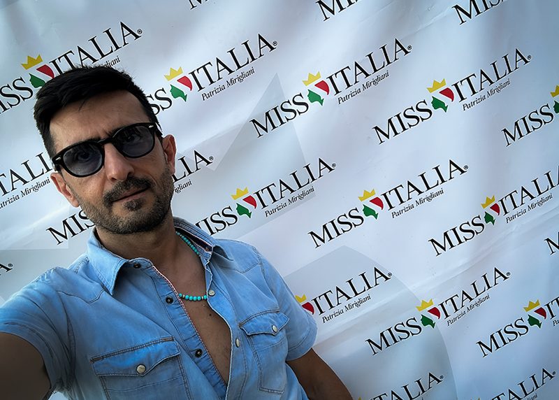 Jespo con gli occhiali da sole davanti al fondale Miss Italia