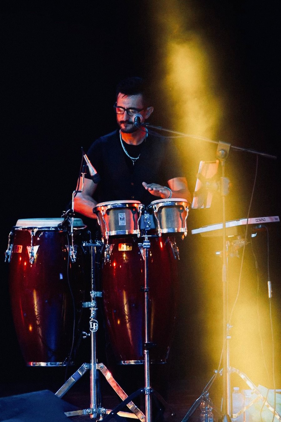 Jespo alle congas durante un concerto, nella luce gialla del palco